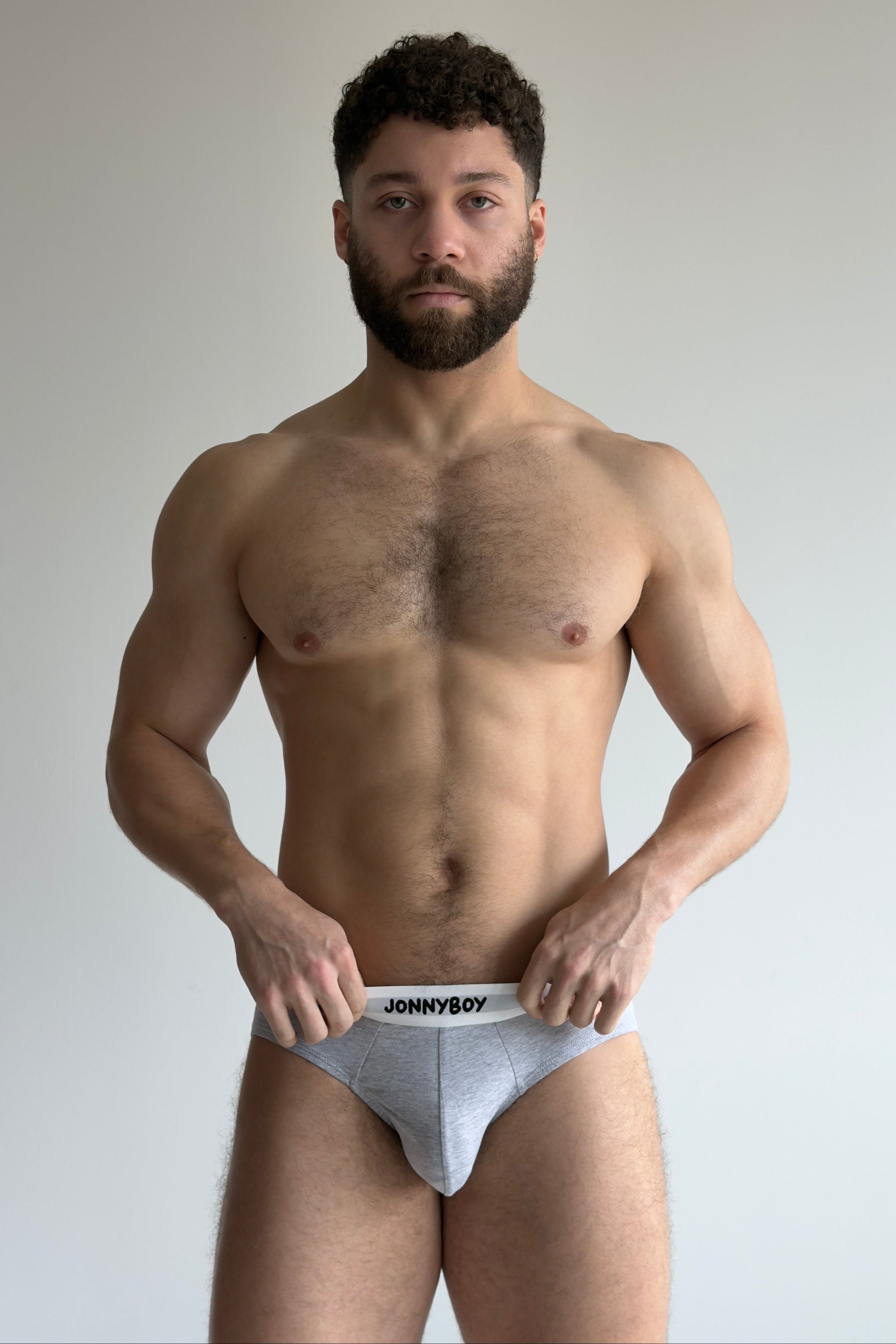 Man holding a pair of underwear with 'Johnny Boy' branding against a plain background